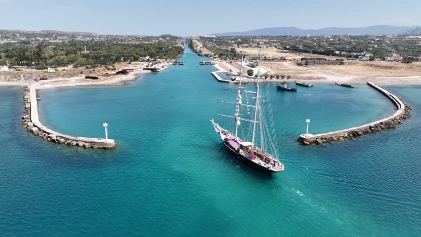 Aerial drone cinematic video of classic sailing boat crossing narrow Corinth canal of Isthmus from West submersible bridge and narrow opening of Corinthian gulf to Saronic gulf, Loutraki, Greece