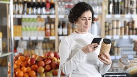 Woman gets acquainted with food scan QR code, take reading canned beans label using phone camera in shop. Client view kidney bean package, inspect manufacturer information using mobile application - Powered by Shutterstock - Get 15% off with code: PIKWIZARD15