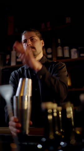 A focused bartender in a dimly lit lounge shaking a stainless cocktail shaker behind the bar, surrounded by shelves of bottles, capturing the craft and motion of mixology