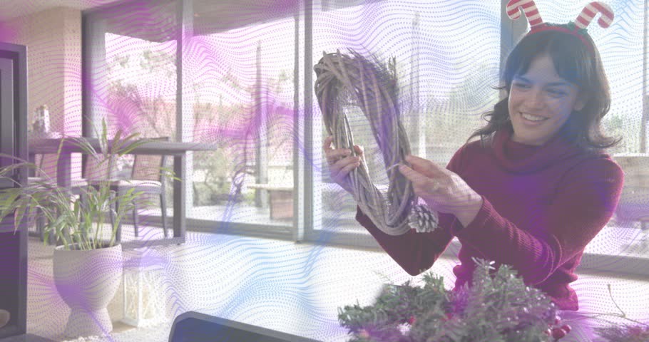 woman crafting holiday wreath in sunroom, tying twine around pinecone and hanging red ornament. Crafting, interior, rustic, seasonal, decorations, diy, cozy