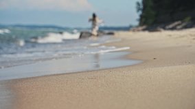 Young woman runs barefoot on sandy shore beside Baltic Sea in Russia. Low angle view highlights foamy water washing onto beach with blurred woman and green forest background under soft daylight - Powered by Shutterstock - Get 15% off with code: PIKWIZARD15