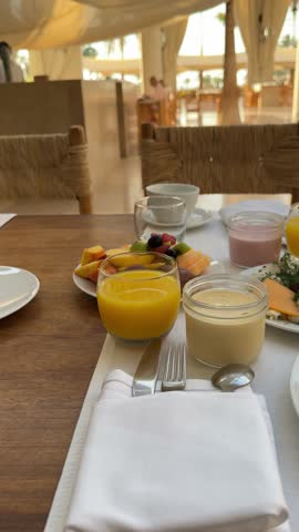  breakfast setting in a restaurant or hotel. There is a glass of orange juice, a plate with an omelette on toast, a salad plate with fresh vegetables, and a plate of appetizers. The interior features 