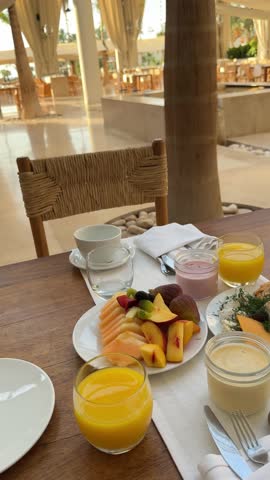  breakfast setting in a restaurant or hotel. There is a glass of orange juice, a plate with an omelette on toast, a salad plate with fresh vegetables, and a plate of appetizers. The interior features 