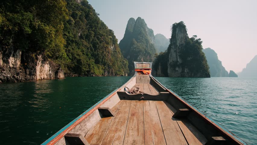 Wooden boat cruising on turquoise water of lake cheow lan amidst stunning limestone karsts and lush jungle in khao sok national park, Thailand