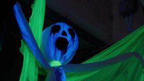 Frightening blue and green ghost decoration with a skull face hanging from the ceiling and glowing under a black light, creating a scary and haunted atmosphere for a halloween party - Powered by Shutterstock - Get 15% off with code: PIKWIZARD15