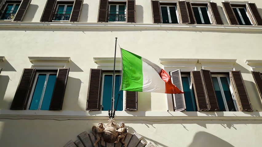 The Italian tricolor flag waves gracefully on the facade of a historic government building in Rome. Bright sunlight illuminates the architecture, symbolizing national pride and Italian heritage.