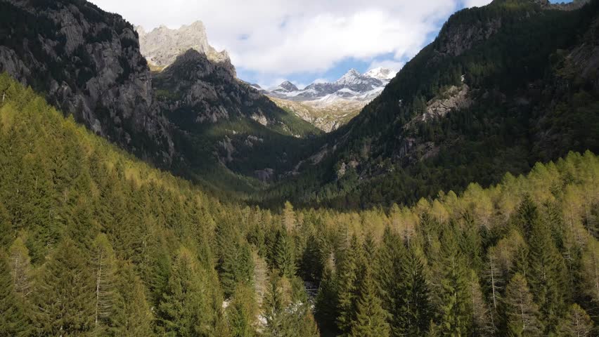 Aerial pullback view of a rugged mountain and boulders covered in pine trees in Val di Mello, Italy. Alpi Retiche, in Val Masino, Valsassina, Italia, flight over torrent with drone. Lake from above.