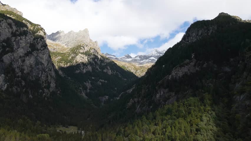 Aerial pullback view of a rugged mountain and boulders covered in pine trees in Val di Mello, Italy. Alpi Retiche, in Val Masino, Valsassina, Italia, flight over torrent with drone. Lake from above.