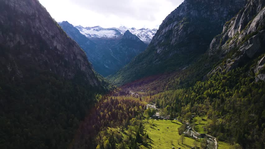 Aerial pullback view of a rugged mountain and boulders covered in pine trees in Val di Mello, Italy. Alpi Retiche, in Val Masino, Valsassina, Italia, flight over torrent with drone. Lake from above.