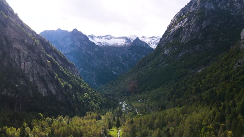 Aerial pullback view of a rugged mountain and boulders covered in pine trees in Val di Mello, Italy. Alpi Retiche, in Val Masino, Valsassina, Italia, flight over torrent with drone. Lake from above.