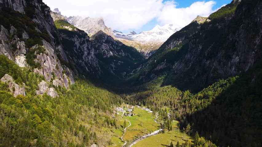 Aerial pullback view of a rugged mountain and boulders covered in pine trees in Val di Mello, Italy. Alpi Retiche, in Val Masino, Valsassina, Italia, flight over torrent with drone. Lake from above.