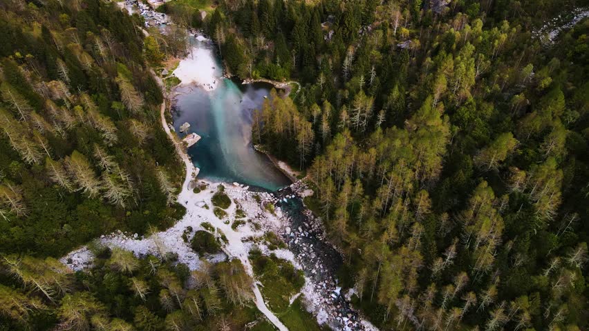 Aerial pullback view of a rugged mountain and boulders covered in pine trees in Val di Mello, Italy. Alpi Retiche, in Val Masino, Valsassina, Italia, flight over torrent with drone. Lake from above.