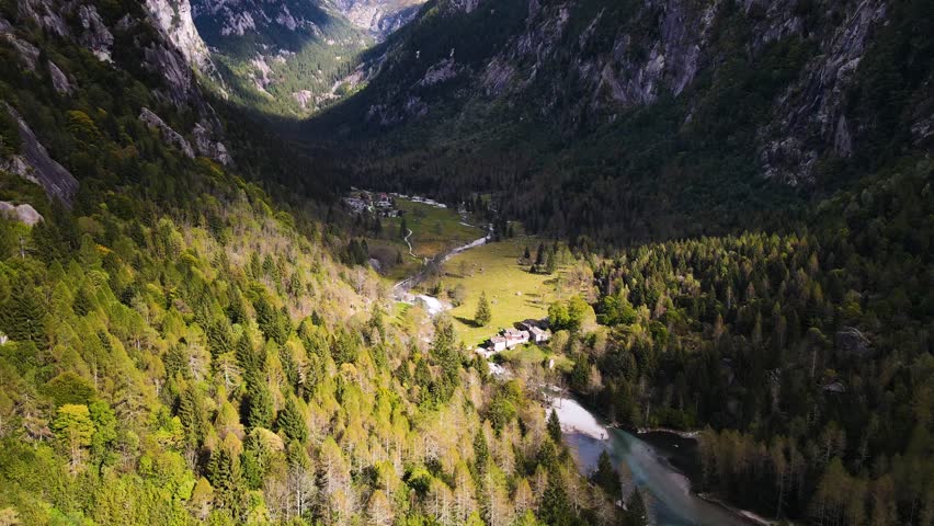 Aerial pullback view of a rugged mountain and boulders covered in pine trees in Val di Mello, Italy. Alpi Retiche, in Val Masino, Valsassina, Italia, flight over torrent with drone. Lake from above.