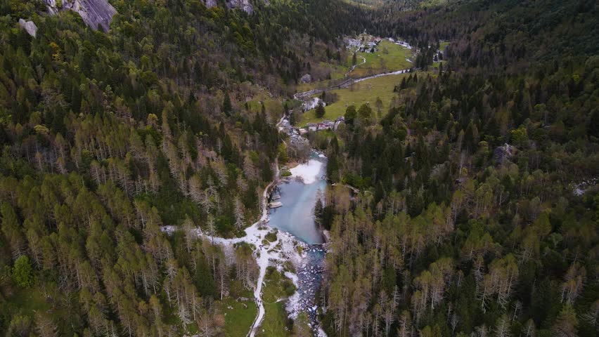 Aerial pullback view of a rugged mountain and boulders covered in pine trees in Val di Mello, Italy. Alpi Retiche, in Val Masino, Valsassina, Italia, flight over torrent with drone. Lake from above.
