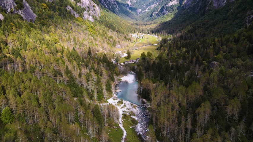 Aerial pullback view of a rugged mountain and boulders covered in pine trees in Val di Mello, Italy. Alpi Retiche, in Val Masino, Valsassina, Italia, flight over torrent with drone. Lake from above.
