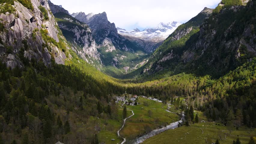 Aerial pullback view of a rugged mountain and boulders covered in pine trees in Val di Mello, Italy. Alpi Retiche, in Val Masino, Valsassina, Italia, flight over torrent with drone. Lake from above.