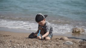Little boys on a rocky beach play with stones and coarse sand. Happy child playing with sand and stones sitting on the seashore.  - Powered by Shutterstock - Get 15% off with code: PIKWIZARD15