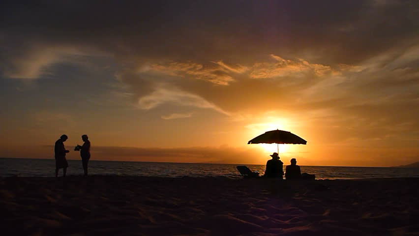 Man and woman couples taking photos and sitting under umbrella along sandy beach