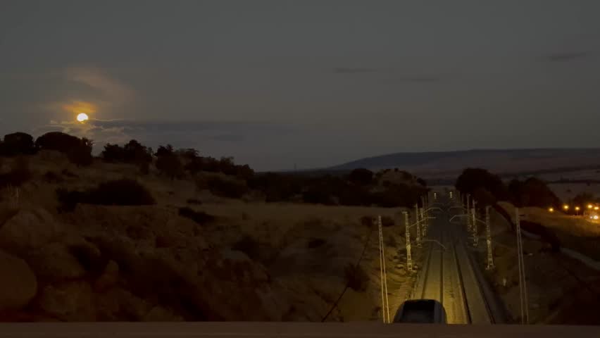A passenger train glides along the tracks under the glow of the Hunter’s Moon rising above the hills of Ávila, Castilla y León, Spain.