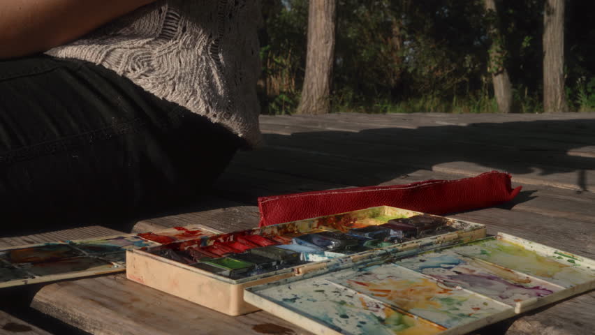 Close-up, the artist's hand with a brush takes watercolor paint from the palette