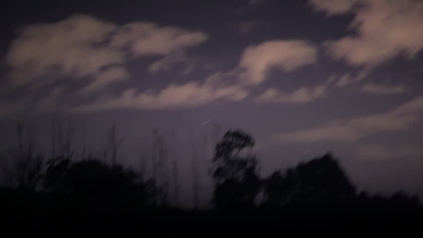 Motion blur of trees and cloudy sky during night drive through rural forest area, illuminated from headlights, dark natural scene with movement and atmospheric light
