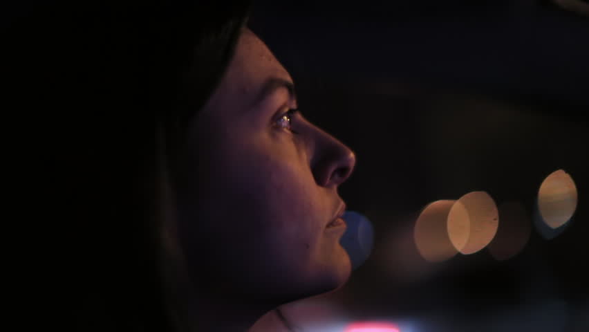 Close up profile of Latina woman driving at night with focused expression, bokeh lights outside car window, interior vehicle perspective during city commute