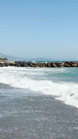 Resting on the beach with stormy turquoise waves of the sea in Almunecar, Spain, under dramatic skies and strong surf.