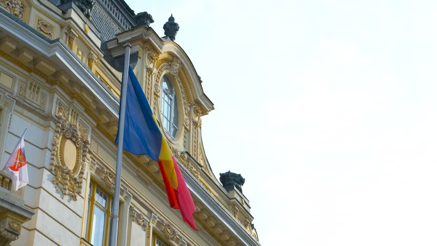 Romanian flag waving proudly on the side of a government building, showcasing national identity and patriotism against a backdrop of blue sky and vibrant colors