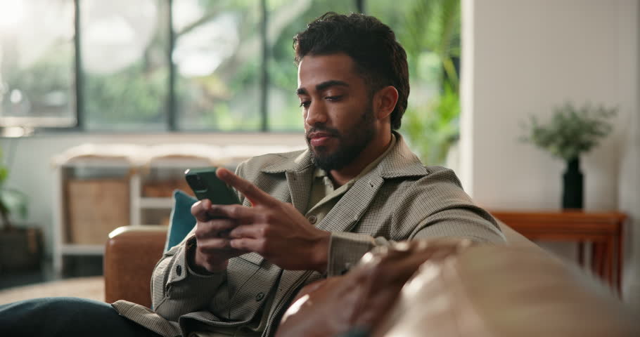 Break, phone and smile with man on sofa in living room of home for relax or social media browsing. App, contact and typing with person in apartment for communication, me time or text message