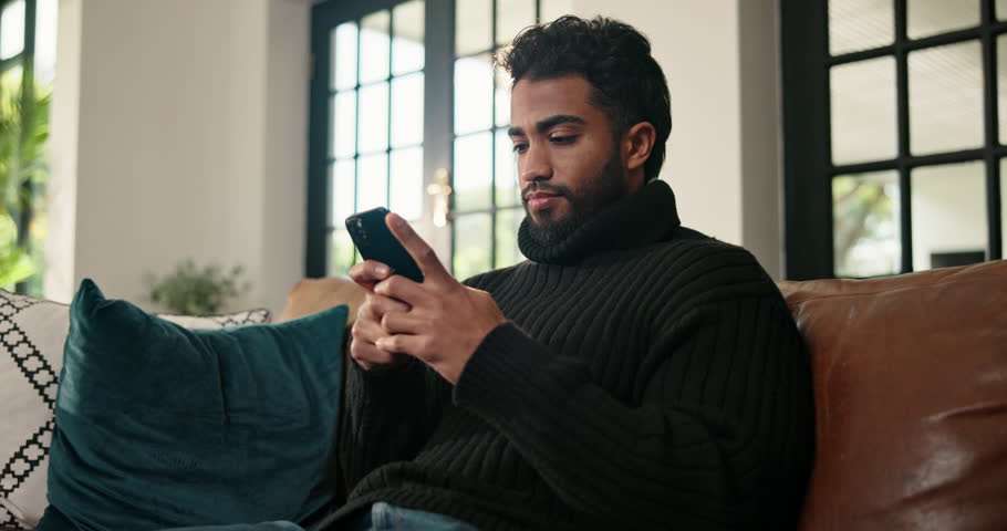 Laughing, phone and text message with man on sofa in living room of home for relax or social media browsing. App, break and typing with funny person in apartment for communication or me time