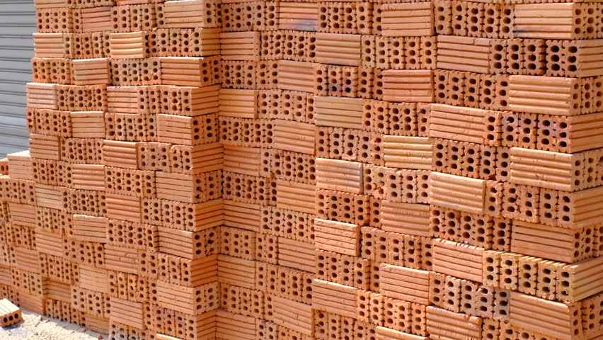 A wall of bricks is piled up in a heap. The bricks are brown and have a rough texture. The wall is made up of many bricks, and it is a large structure