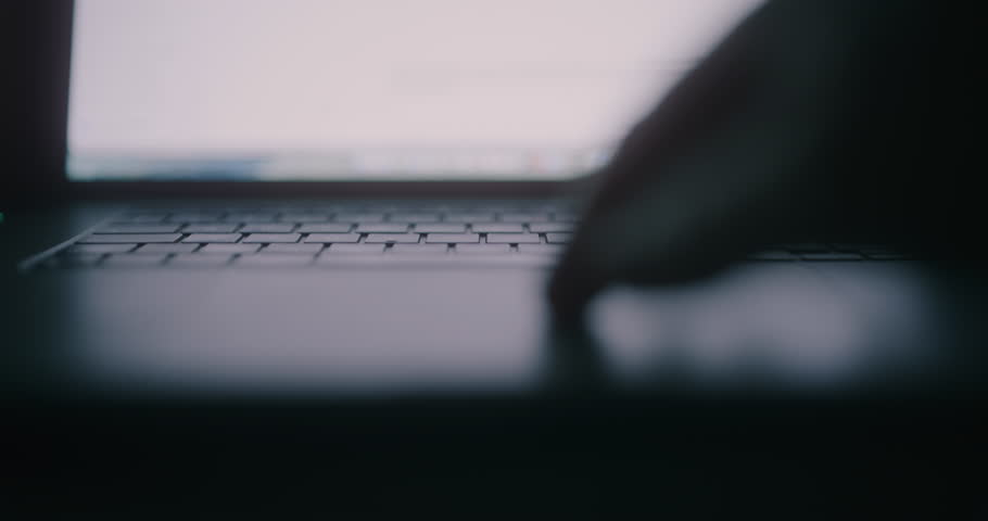 Close-up silhouette of hands typing on a laptop keyboard at night, showcasing work on the computer.
