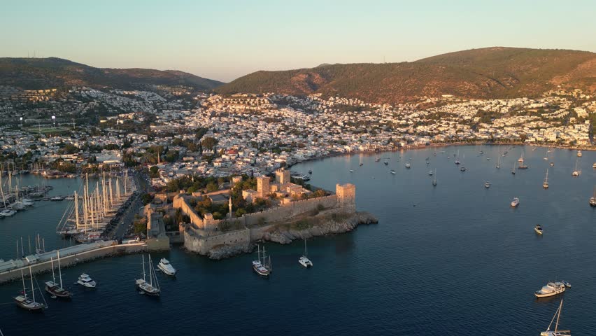 Bodrum, Turkey: Aerial drone footage of sunset over castle in Bodrum. Taken with rotating motion, showing the yachts docking in marina, city landscape, and mountain in the background