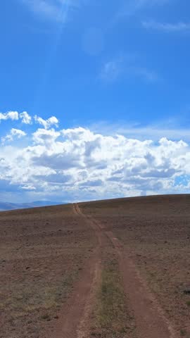 Vertical video of a car driving along a country road under blue sky. Altai desert and semi-desert environment.
