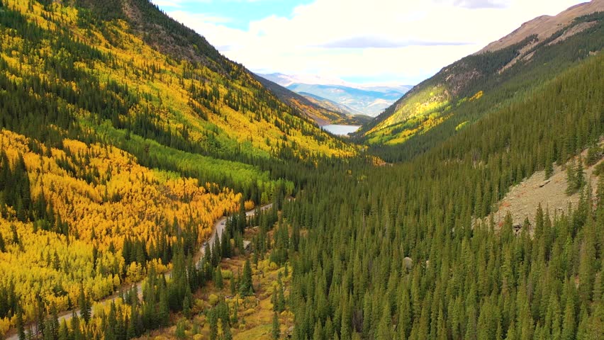 Idaho’s Sawtooth Range gleams under autumn sunlight as lakes reflect golden forests and narrow roads wind through rugged alpine landscapes.
