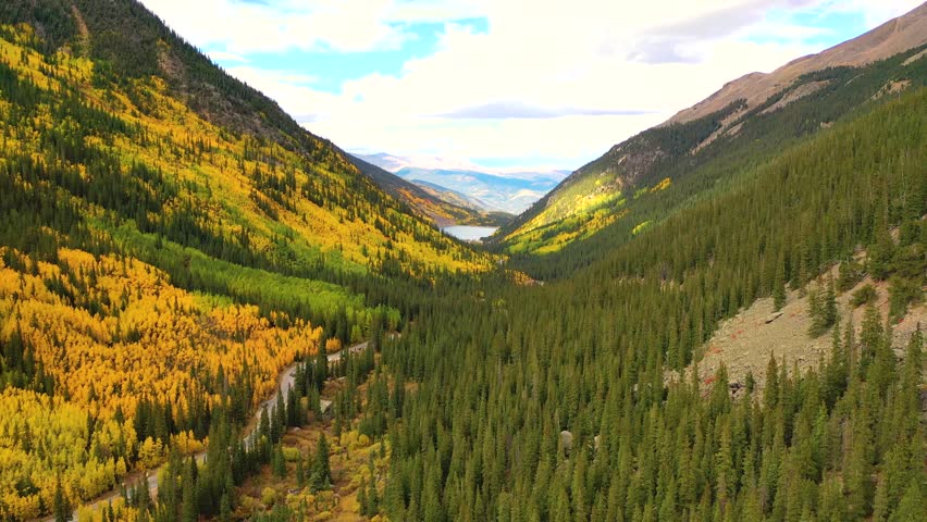 The Teton Range in Wyoming glows with fall color as aspen forests and winding rivers stretch toward snow-covered peaks under a bright blue sky.