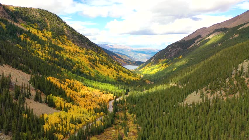 The Sierra Nevada mountains in California glow with fall color as bright trees line the ridges and cars follow curving roads through rocky forest slopes.