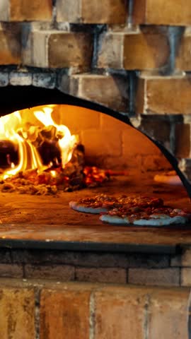 chef using a peel to move a pizza closer to the fire for even baking in a traditional wood-fired brick oven - slow motion vertical