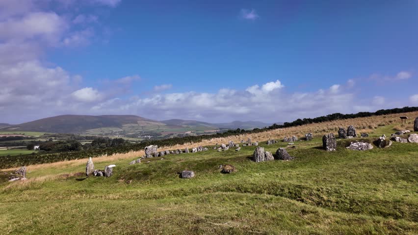 Iron Age roundhouse remains visible on a grassy hillside under a blue sky. slow pan left