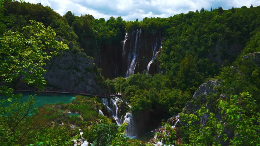 Waterfall flowing into turquoise lakes surrounded by lush forest in Plitvica National Park, Croatia