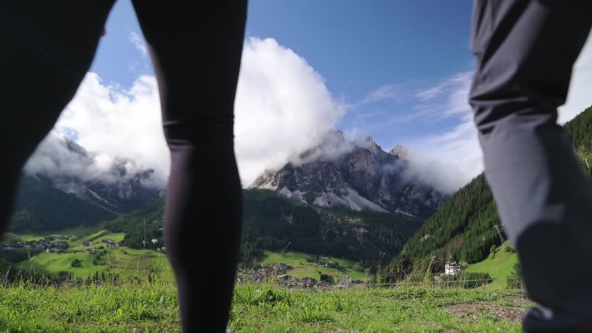 Couple holding hands walking in the green valley of the Dolomites with scenic mountain view