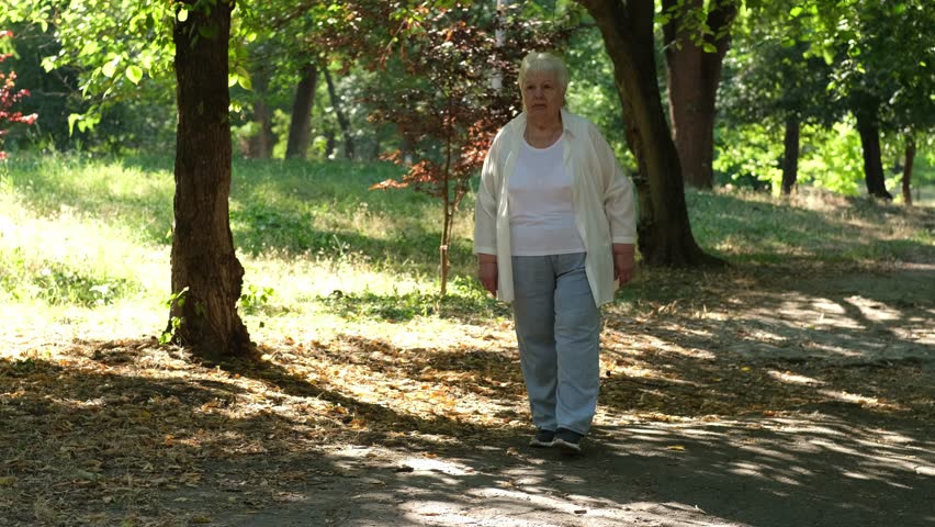 Senior woman feels pain while walking in park in summer. Old lady touching back by hands, having backache, muscle, hip pain outdoors. Elderly people suffering from waist pain 