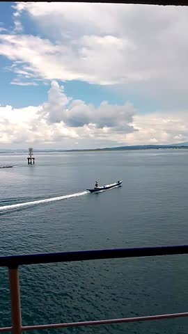 Boat Cruising on Calm Ocean Waters with Distant Offshore Platform Under Blue Sky