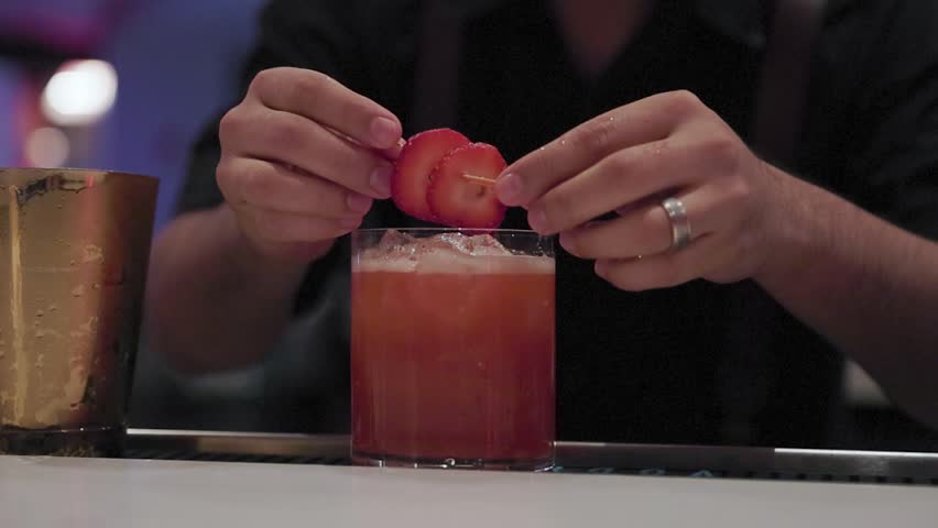 A person places fresh strawberries on a cocktail as garnish.
