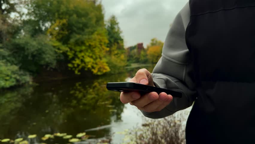 A man drinks coffee with a phone in his hands in an autumn park.