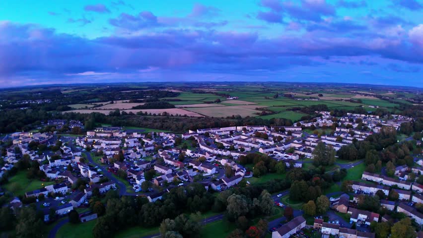 Aerial view of a peaceful residential town at sunset, surrounded by fields and farmland. Blue hour tones blanket the sky and landscape in this scenic rural community