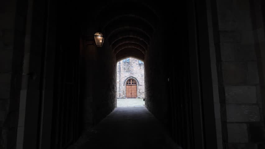 Dark castle archway creating a path to an ancient building and bright courtyard.POV