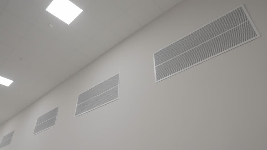 A low-angle shot of the large HVAC ventilation vents on the wall of a sterile data center, laboratory, or cleanroom, highlighting the critical climate control system.