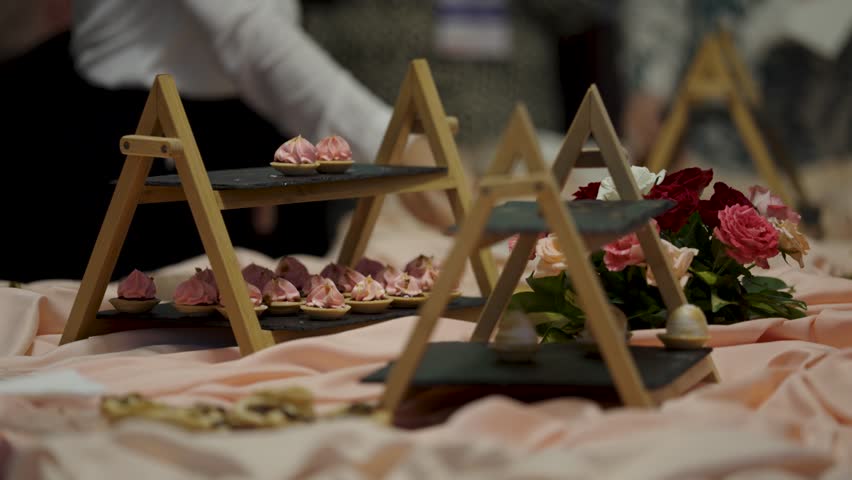 A beautiful display of delicate pink pastries on modern, tiered serving stands made of wood and slate. This elegant dessert table is ready for guests at a wedding, gala, or corporate event.