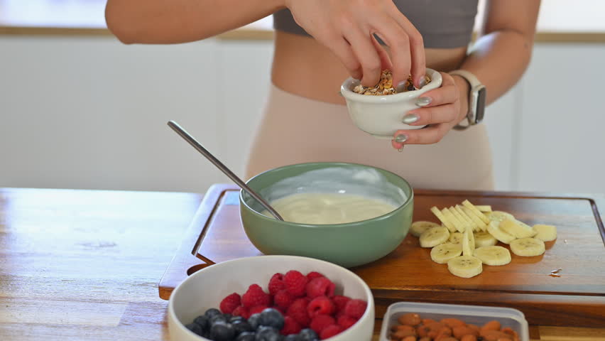 Fitness woman making a wholesome yogurt bowl with fresh fruits and granola for a healthy meal.